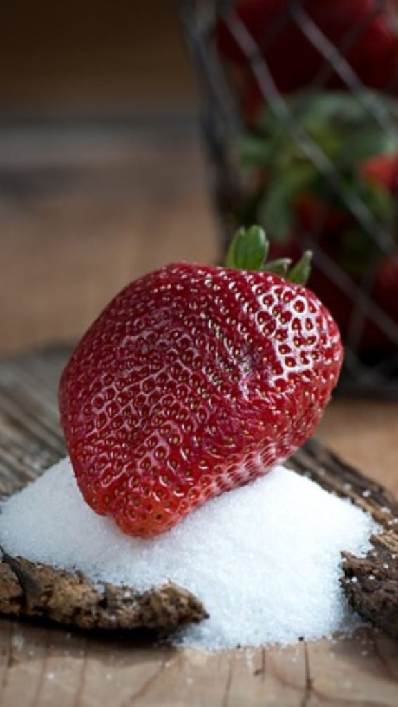 Red strawberry on wooden piece with icing sugar and strawberry basket blurred in the back strawberry phone wallpaper