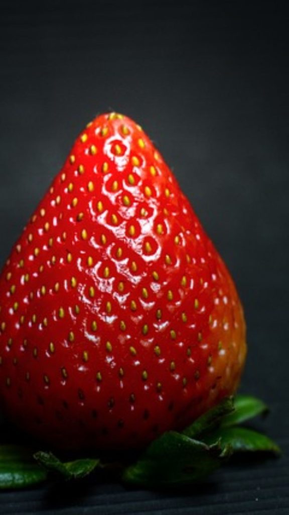 Velvety red strawberry zoomed photograph with black background strawberry phone wallpaper