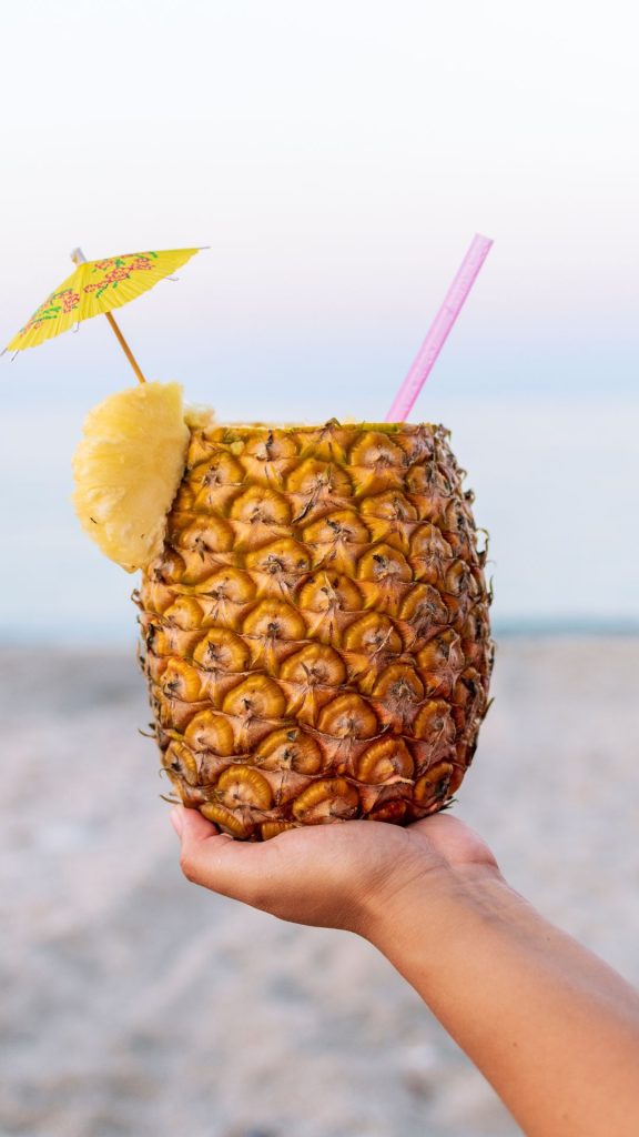 Fresh pineapple juice in pineapple with straw and cocktail umbrella with beach background Pineapple wallpaper