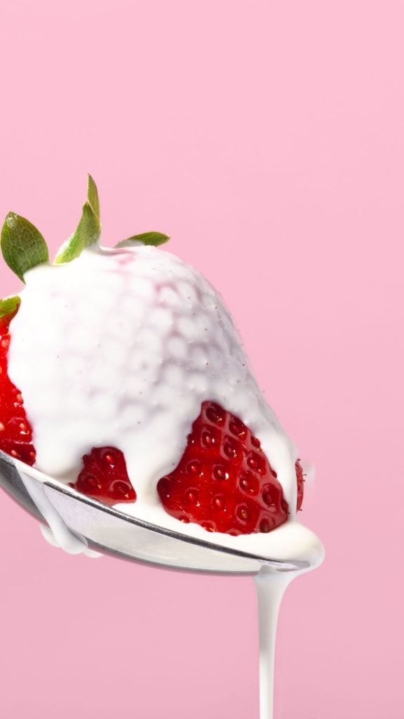 Red strawberry in spoon with cream Strawberry Background Wallpaper