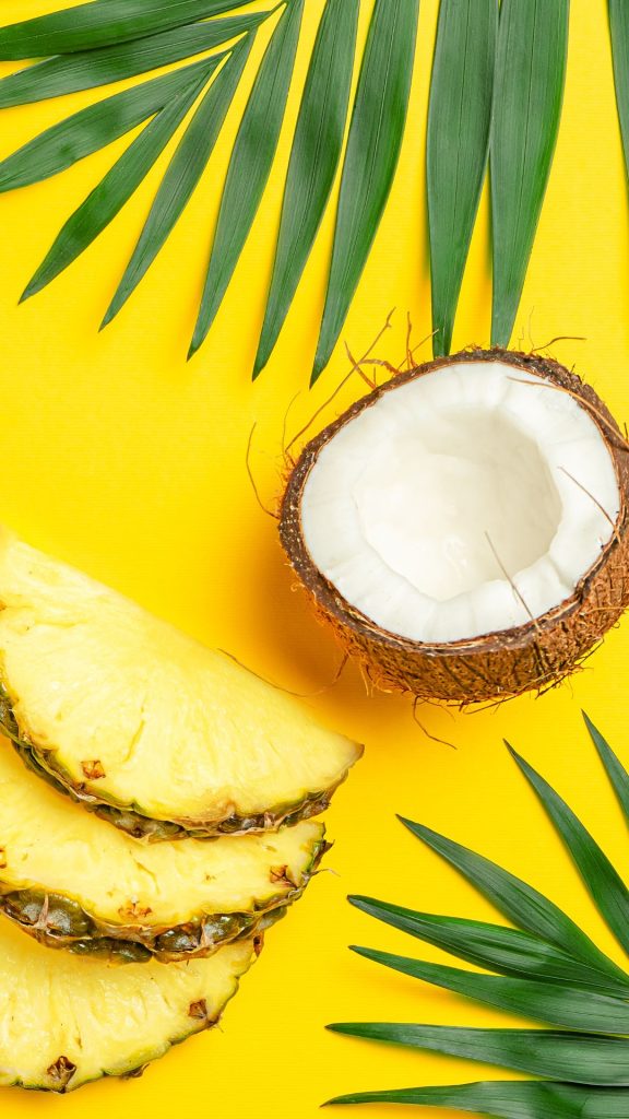 Sweet pineapple pieces with coconut and big green leaves on yellow background Pineapple wallpaper
