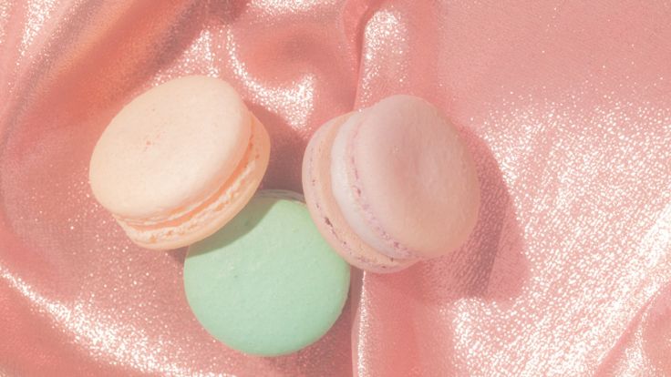 Pastel macarons resting on a shimmering pink satin fabric pink wallpaper