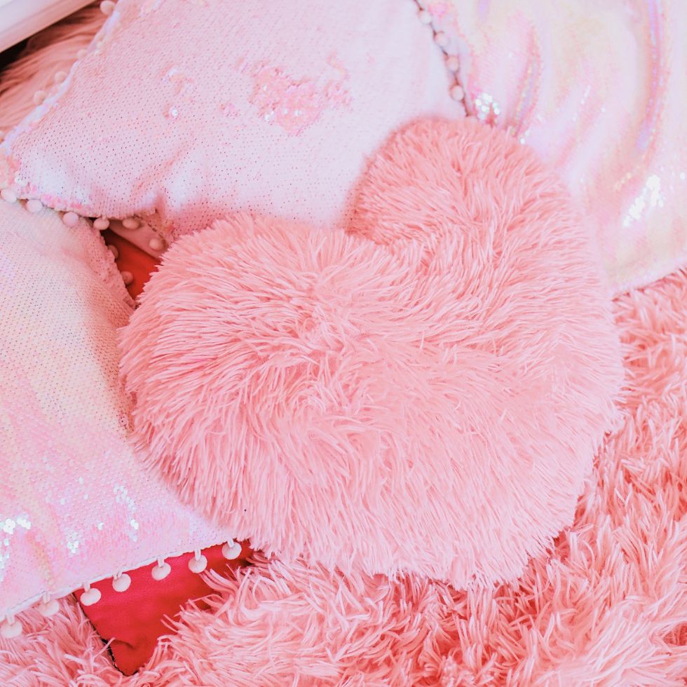 Fluffy pink heart shaped pillow on a fuzzy shag rug pink wallpaper