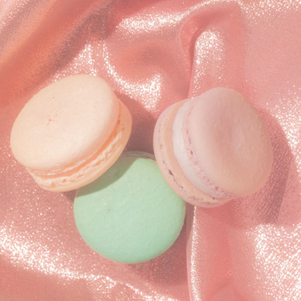 Three colorful French macarons resting on shimmering pink satin fabric pink wallpaper