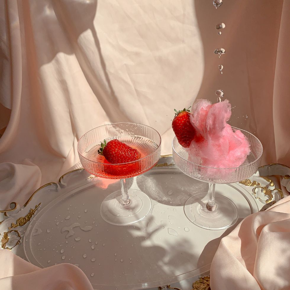 Two elegant glass coupes with strawberries and pink cotton candy on a decorative tray pink wallpaper