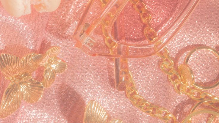 Gold butterfly clips and jewelry on shimmering pink fabric, preppy wallpaper.