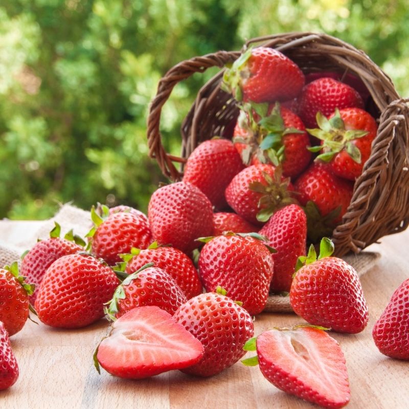 A basket of fresh strawberries sits on a rustic wooden table